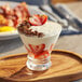 A glass of Oikos Pro Fat-Free Vanilla Greek yogurt topped with strawberries on a wooden tray.