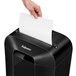 A hand putting a paper into a Fellowes LX70 paper shredder.