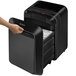 A hand opening a black Fellowes Powershred LX210 paper shredder.