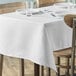 A white rectangular table cover on a table with plates and glasses.