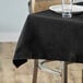 A black Choice square table cover with a white plate and glass on a table.