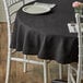 A table with a black 90" round Choice tablecloth and white chairs.