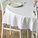A white table with a Choice white round tablecloth and flowers on it.