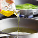 A hand pouring Molivo olive pomace oil into a pan of green beans.