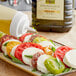 A Colavita Mediterranean Extra Virgin Olive Oil bottle being poured onto a plate of tomatoes, mozzarella, and basil.