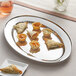 An Acopa stainless steel oval platter with food and a glass of wine on it.