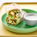 A green plate with tortilla wraps of Rebellyous Kickin' Chicken Tenders and white bowl of dip.