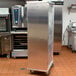 A large metal box on wheels for sheet pans in a school kitchen.