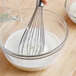 A whisk being whisked into a bowl of milk.