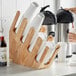 A person holding a coffee cup and using a Acopa wood cup holder on a counter with a stack of white cups in it.
