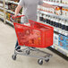 A man shopping at a grocery store pushes a red Regency plastic grocery cart.