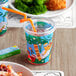 A plastic Choice jungle print kid's cup with a straw in it on a table with a plate of food.