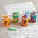 A group of Choice plastic kid's cups with straws and a dinosaur design on them on a table with a coloring book.