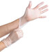 A pair of clear disposable vinyl gloves being worn on hands.