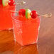Two clear Fineline Tiny Tumblers filled with red liquid with fruit on a stick.