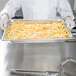 A person holding a Vollrath stainless steel tray of french fries.