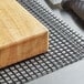 A wood block on a black mesh shelf liner.