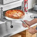 A person using a Choice aluminum pizza peel to put a pizza in the oven.