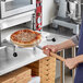 A person using a Choice aluminum pizza peel with a wooden handle to put a pizza in a pizza oven.