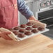 A person holding a tray of muffins made in a Choice aluminum muffin pan.
