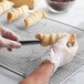 A person using an Ateco cream roll mold to cut a pastry.