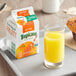 A carton of Tropicana Pure Premium orange juice next to a glass of orange juice and a muffin.