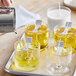 A tray of Acopa cylindrical glass votive candle holders filled with yellow liquid.