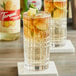 Two glasses of Torani Puremade Ginger Syrup flavored drinks with ice and lime slices on a white coaster.