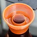 A Fineline plastic cup with an orange lid filled with liquid and a small round orange object.