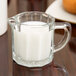 An Anchor Hocking glass creamer filled with milk on a table.