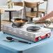 A woman uses an Avantco double burner hot plate to cook food on a table.