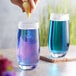 A hand squeezing a lemon into a glass of blue Wild Hibiscus Butterfly Pea flower liquid.