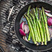 A de Buyer Blue Carbon Steel perforated fry pan with asparagus and onions cooking on a grill.