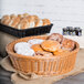 A round honey plastic basket filled with baked goods on a table in a bakery display.