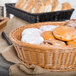 A round honey plastic basket filled with donuts and bread on a table in a bakery display.