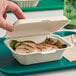 A hand holding an EcoChoice Natural Bagasse Take-Out Container filled with food.