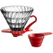 A Hario V60 red glass coffee dripper with a plastic measuring spoon.