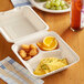 An EcoChoice bagasse take-out container with food and utensils on a table.