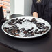 A woman holding an American Metalcraft aluminum seafood tray of mussels on ice.