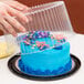 A person using a D&W Fine Pack plastic cake container to cover a blue cake on a table.