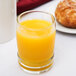A close up of a Libbey Cascade beverage glass filled with orange juice on a table with a donut.