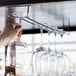 A person using a Regency chrome plated glass hanger rack to hold wine glasses over a bar.