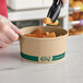 A hand using black tongs to fill a round EcoChoice compostable take-out container with churros.