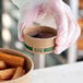 A hand holding a brown EcoChoice round Kraft compostable container filled with churros.