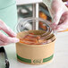 A plastic gloved hand placing a EcoChoice compostable lid on a container of food.