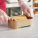 A person in gloves holding a piece of food in a rectangular cardboard container.