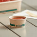 A small EcoChoice paper take-out container of red sauce on a table.