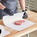 A person in black gloves cutting a piece of raw meat on a cutting board using Choice white butcher paper.