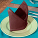 A folded Intedge burgundy polycotton napkin on a plate.