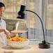 An Avantco black single arm flexible heat lamp over a table with a woman holding a plate of food.